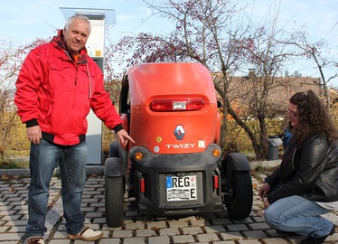  - Bernhard Grote zeigt auf sein Kennzeichen, das nun ein E ziert. Christa Bushi (re.) hat zuvor die TÜV-Plakette und die Zulassung angebracht. Foto: Langer/Landkreis Regen