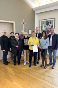 Alle freuen sich mit Sieglinde Gens (6.v.li. im gelben Pulli), v.li.: Pfarrer Tobias Magerl, Maria Hanninger, Jutta Müller-Dietz, Waltraud Weindl, Martha Heimerl, Landrat Dr. Ronny Raith, Claudia Stiglbauer und Bürgermeister Richard Gruber. Foto: Heiko Langer / Landratsamt Regen