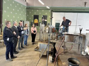 Bürgermeister Fritz Schreder (v.li.), Landrat Dr. Ronny Raith, Eberhard Eisch, Julia Eisch und Wirtschaftsförderin Teresa Sitzberger ließen sich am Studioofen von Glasmacher Robert Stadler zeigen, wie buntes Glas geblasen wird. Foto: Heiko Langer / Landratsamt Regen