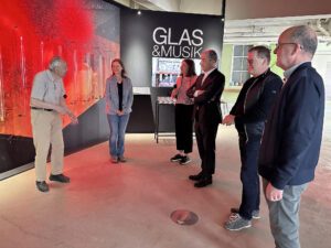 Der 95-jährige Alfons Eisch (v.li.) zeigte Julia Eisch, Wirtschaftsförderin Teresa Sitzberger, Landrat Dr. Ronny Raith, Bürgermeister Fritz Schreder und Eberhard Eisch, wie Musik aus Glasinstrumenten klingt. Foto: Heiko Langer / Landratsamt Regen