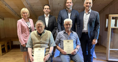 Ein Gruppenbild als Erinnerung: Die Geehrten Konrad Edenhofer (li.) und Herbert Weinberger dürfen Platz nehmen. Es gratulierten, v. li.: Bürgermeisterin Gaby Wittenzellner (Achslach), Vermessungsamtschef Matthias Holstein, Bürgermeister Josef Saller (Gotteszell) und Landrat Dr. Ronny Raith. Foto: Heiko Langer / Landratsamt Regen