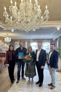Max Schweikl (2. v.li.) präsentiert den Award. Landrat Dr. Ronny Raith (4. v.li.) überreichte einen Blumenstrauß an Dagmar Schweikl. Wirtschaftsförderin Teresa Sitzberger und Bürgermeister Jochen Koller schlossen sich den Glückwünschen an. Foto: Heiko Langer / Landratsamt Regen