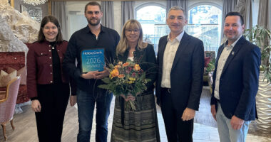 Max Schweikl (2. v.li.) präsentiert den Award. Landrat Dr. Ronny Raith (4. v.li.) überreichte einen Blumenstrauß an Dagmar Schweikl. Wirtschaftsförderin Teresa Sitzberger und Bürgermeister Jochen Koller schlossen sich den Glückwünschen an. Foto: Heiko Langer / Landratsamt Regen