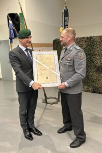 Kommandeur Sean Papendorf überreichte das grüne Barett und die Ernennungsurkunde an Landrat Dr. Ronny Raith. „Ich weiß, dass Du normalerweise das blaue Barett der San-Einheit trägst, vielleicht können wir Dich nun vom grünen überzeugen“, sagte Papendorf mit Blick auf Raiths Bundeswehrvergangenheit als Sanitätsoffizier. Foto: Heiko Langer / Landratsamt Regen