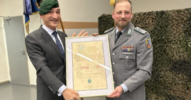 Kommandeur Sean Papendorf überreichte das grüne Barett und die Ernennungsurkunde an Landrat Dr. Ronny Raith. „Ich weiß, dass Du normalerweise das blaue Barett der San-Einheit trägst, vielleicht können wir Dich nun vom grünen überzeugen“, sagte Papendorf mit Blick auf Raiths Bundeswehrvergangenheit als Sanitätsoffizier. Foto: Heiko Langer / Landratsamt Regen