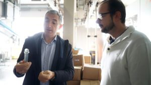 Gemeinsamer Blick aufs Röhrchen: Ludwig M. Plöchl erläutert Landrat Dr. Ronny Raith, wie aus einem PET-Rohling eine Flasche wird. Foto: Miriam Lange / Landratsamt Regen.