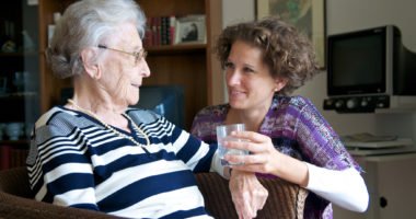 Seniorin wird ein Glas Wasser gereicht