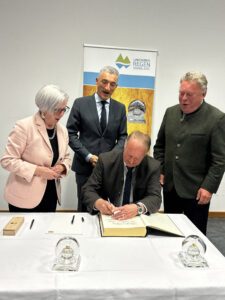 Landrat Dr. Ronny Raith (stehend Bildmitte) freut sich. Willi Killinger trägt sich ins Goldene Buch des Landkreises ein. Zuvor hatten dies schon Rita Röhrl (li.) und Helmut Brunner gemacht. Foto: Heiko Langer / Landratsamt Regen