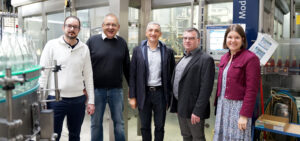 Erfrischend sympathisch: Landrat Dr. Ronny Raith (3. v. r.), Kirchdorfs Bürgermeister Alois Wildfeuer (2. v. r.), Wirtschaftsreferentin Teresa Sitzberger (1. v. r.) und das Geschäftsführerduo Ludwig Plöchl (2. v. l.) und Ludwig M. Plöchl (1. v. l.) bei der Abfüllung von Libella Apfel-Johannisbeerschorle. Foto: Miriam Lange / Landratsamt Regen.