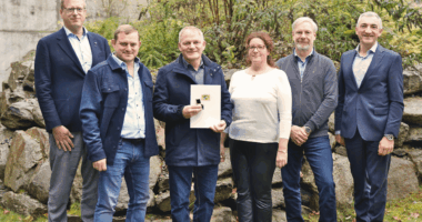 Ehrung nicht am Pfahl, aber vor Naturstein: Landrat Dr. Ronny Raith (rechts) überreichte Matthias Rohrbacher (3. v. li.) im Landratsamt Regen die goldene Dienstzeitenauszeichnung des Bayerischen Naturschutzdienstes. Mit dabei waren (v. li.) Regierungsdirektor Alexander Kraus (Abteilungsleiter Kommunal-, Bau- und Umweltrecht), Hans Günther Knogl (3. Bürgermeister von Grafling) sowie Uwe Behringer und Elisabeth Schröder vom Umweltamt des Landkreises Regen. Foto: Miriam Lange / Landkreis Regen.