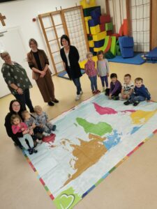 Einmal um die Welt mit einem Schritt: Die Kinder der Eine Welt-Kita St. Josef erkunden gemeinsam mit ihrem Team die neue Weltspielplane – ein Geschenk des Fairtrade-Landkreises und des Fachbereichs Klimaschutz und Nachhaltigkeit. Rechts im Bild Kita-Leitung Elfriede Hartl, daneben Nachhaltigkeitskoordinatorin Teresa Raith. Foto: Jessica Olbrich.