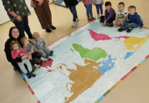 Einmal um die Welt mit einem Schritt: Die Kinder der Eine Welt-Kita St. Josef erkunden gemeinsam mit ihrem Team die neue Weltspielplane – ein Geschenk des Fairtrade-Landkreises und des Fachbereichs Klimaschutz und Nachhaltigkeit. Rechts im Bild Kita-Leitung Elfriede Hartl, daneben Nachhaltigkeitskoordinatorin Teresa Raith. Foto: Jessica Olbrich.