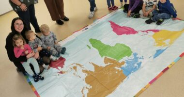 Einmal um die Welt mit einem Schritt: Die Kinder der Eine Welt-Kita St. Josef erkunden gemeinsam mit ihrem Team die neue Weltspielplane – ein Geschenk des Fairtrade-Landkreises und des Fachbereichs Klimaschutz und Nachhaltigkeit. Rechts im Bild Kita-Leitung Elfriede Hartl, daneben Nachhaltigkeitskoordinatorin Teresa Raith. Foto: Jessica Olbrich.