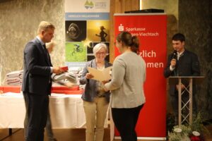 Kreissportbeauftragter Harald Haase und Rita Röhrl überreichen Marion Neubert ihre Auszeichnung, anmoderiert durch Patrick Zens. Foto: Kreisentwicklung Landkreis Regen
